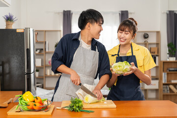 Young couple cooking together in kitchen, smiling and preparing fresh salad bowl