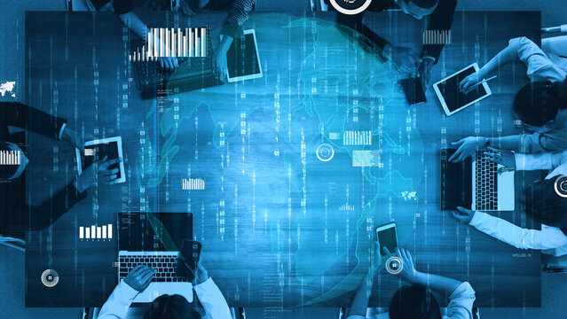 A diverse business team engaged in a digital data analysis session. Laptops and tablets are present on the table, surrounded by global graphics and charts. Xenic