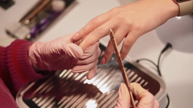 Nail procedure. Salon treatment. Manicure woman master hands filing acrylic fingernails with professional emery board doing beauty for girl client spa.