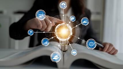 A person interacts with a lightbulb placed on an open book, representing the fusion of innovation and technology, enhanced by digital icons symbolizing data exchange. Crux