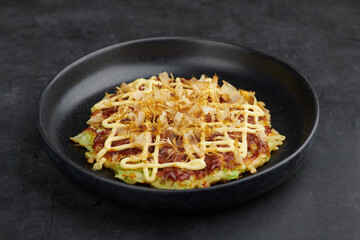 Okonomiyaki with mayo and bonito flakes on black plate, selective focus