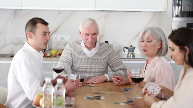 Mature friends is playing card game poker with middle-aged spouses. Married couple pensioners have fun during meeting and gatherings, enthusiastically excitedly fulfill conditions of game with friends