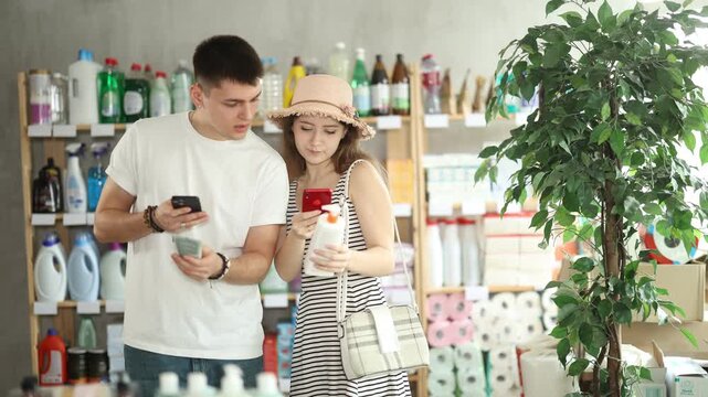 Thoughtful couple buyer scans barcode using application on mobile phone, choose suncreen cream. Customer follows link and reads information about product, data on recycling of packaging