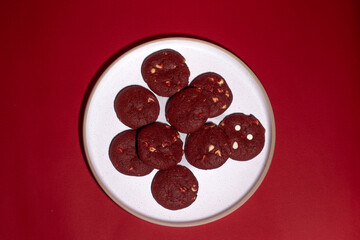 White plate filled with red velvet cookies on a vibrant red background, ideal for Valentine’s Day, romance, and festive dessert themes