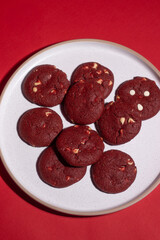 White plate filled with red velvet cookies on a vibrant red background, ideal for Valentine’s Day, romance, and festive dessert themes