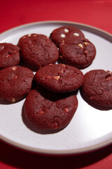 White plate filled with red velvet cookies on a vibrant red background, ideal for Valentine’s Day, romance, and festive dessert themes