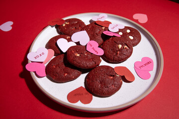 Red velvet cookies decorated with pastel paper hearts and love messages, perfect for Valentine’s Day promotions and romantic visuals