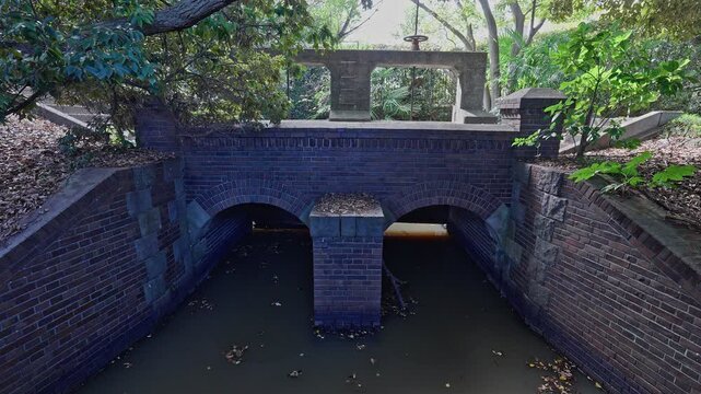 The dark brick culvert of the Jinzaemon Weir with two archways carrying water, leading toward the concrete gate structure.