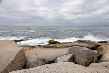 Serene Atlantic view from rocky shores of Peggy's Cove, Nova Scotia, with ocean waves and an overcast sky capturing the rugged coastal beauty.