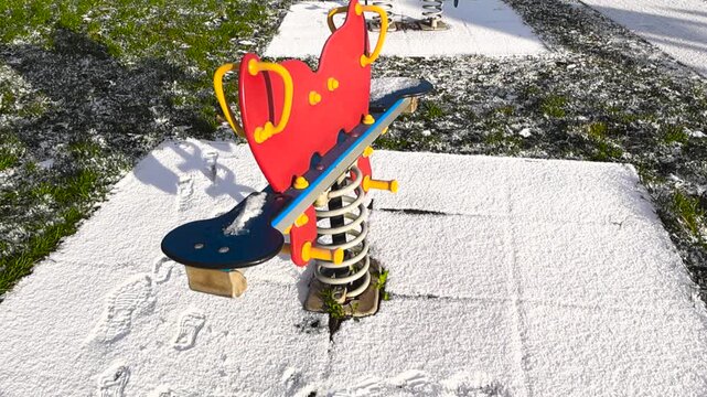 Gorgous and fun vibrant colored spring rider bouncing and wobbling back and fourth at a winter sunny playground with fresh white snow covering it. Green grass still visible from late autumn.
