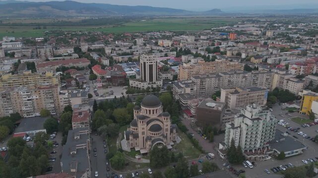 Aerial dusk view of Catedrala Adormirea Maicii Domnului with the softly lit Deva cityscape behind it.
