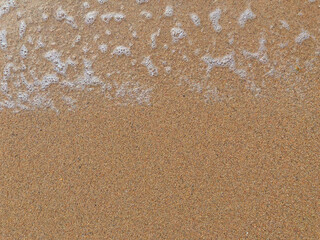 Ocean Wave Foam Edge on Golden Sand Beach Background. Summer Vacation and Travel Concept. Close-up Texture of Sea Water Bubbles and Wet Sand with Copy Space.