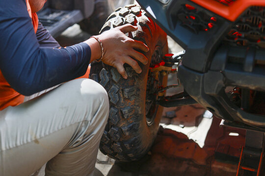 Focused mechanic checking rugged tire on an off road vehicle during race. Man in action repairing wheel with concentration, showing hands on maintenance for motorsport - Powered by Adobe