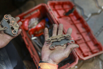 Focused mechanic hand holding dirty worn brake pad from car during repair and maintenance. An automotive professional checking old part with tool box in background