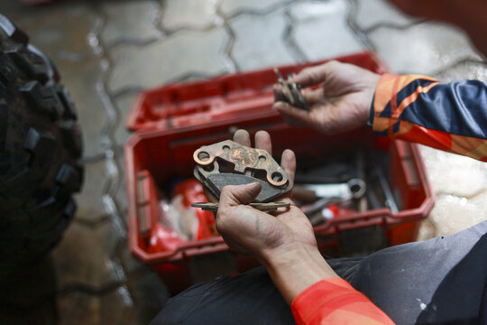 Focused man repairs brake caliper from vehicle. His hands hold part over red toolbox, showing concentration and skill during maintenance work in garage