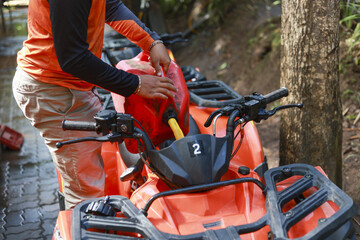 Focused man refueling an orange ATV vehicle with fuel from red gas can. Getting quad ready for an...