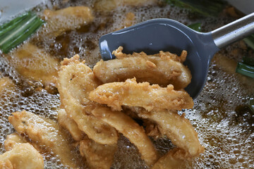 Appetizing closeup of delicious deep fried banana snack cooking in hot oil. Crispy golden brown food bubbling in pan makes for popular but unhealthy street food meal