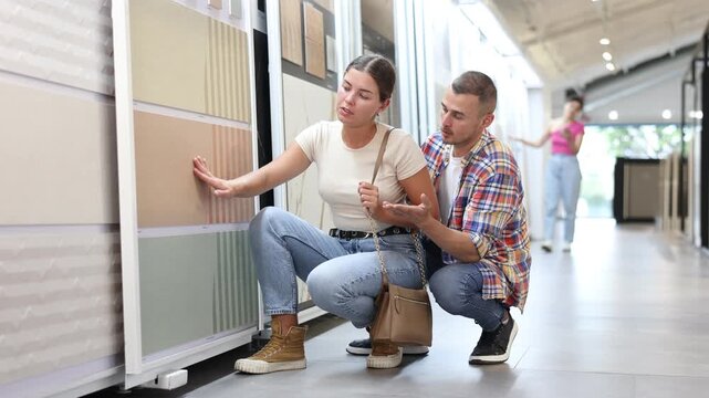 Couple of young man and woman customers selecting tiles from samples in hardware store