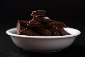 Small pieces of chocolate bars are arranged on a black background