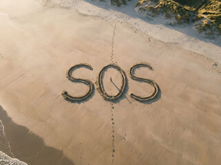giant ‘SOS’ traced in sand on beach, top-down drone view, lone footprints nearby