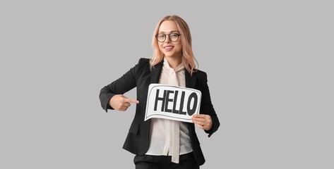 Happy businesswoman pointing at speech bubble with word HELLO on grey background © Pixel-Shot