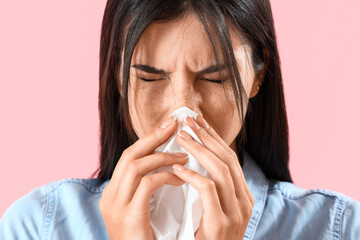 Allergic young woman with tissue sneezing on pink background, closeup
