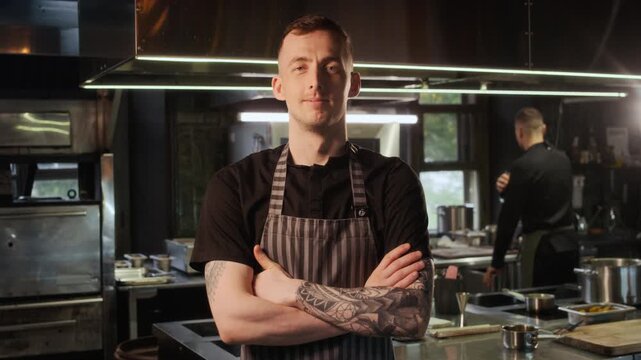 Front view medium shot of confident young chef looking at camera standing in restaurant kitchen and posing with arms crossed, copy space