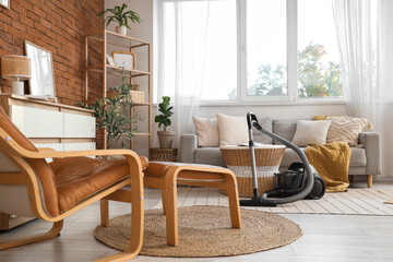 Interior of living room with vacuum cleaner, sofa and armchair