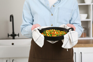 Young woman holding frying pan with roasted vegetables in kitchen