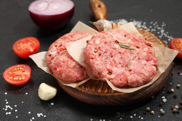 Wooden tray with raw meat cutlets on black grunge background