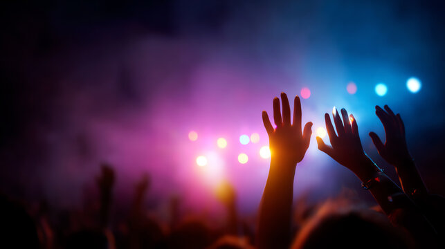 Hands raised in a vibrant concert crowd, illuminated by colorful stage lights and surrounded by atmospheric smoke, capturing the energy and excitement of live music
