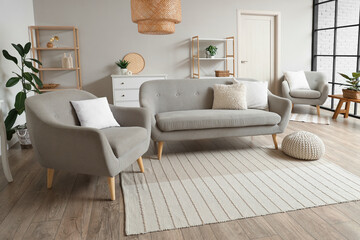 Interior of stylish living room with cozy grey armchair, sofa and pouf