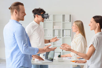 Fototapeta premium Young man using VR glasses with his colleagues in office