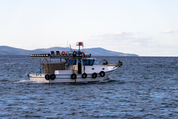 Obraz premium Small Commercial Fishing Boat Moving Across the Open Sea, Flying a Turkish Flag and Creating a Wake Against a Backdrop of Distant Hills.