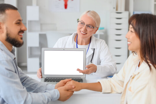Female fertility doctor showing blank laptop to couple after IVF at table in clinic - Powered by Adobe