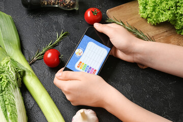 Young woman using meal plan app on mobile phone on black grunge background, closeup