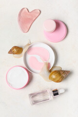 Giant Achatina snails, under-eye patches, guasha tool, bottle and jars of cosmetic products on white grunge background, closeup