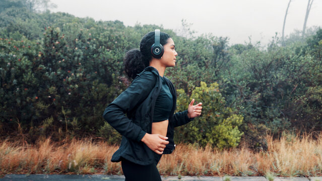 Fitness, woman and running with headphones in road for exercise, music playlist and cardio podcast. Athlete, person and workout in nature with audio streaming, pace training and endurance challenge