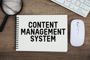 Content Management System text written on notepad with keyboard, optical mouse and magnifying glass on wooden background
