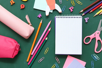 Blank notebook with different stationery supplies on green chalkboard