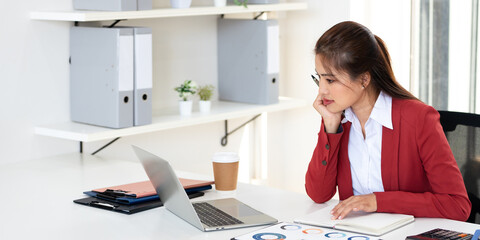 Concentred businesswoman analyzing documents while using laptop in modern office.