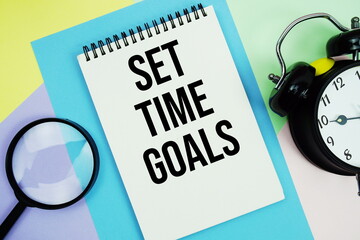 Set Time Goals text written on notepad with alarm clock and magnifying glass on pastel background