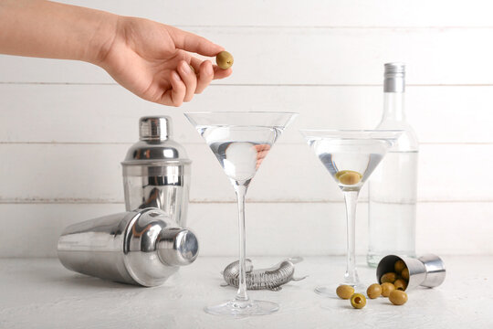 Woman adding green olives into glasses with tasty martini cocktail on light table - Powered by Adobe