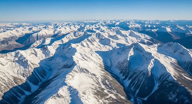 Aerial view of snow-covered mountain range under clear blue sky, capturing the grandeur of winter landscapes and nature, suitable for tourism marketing.