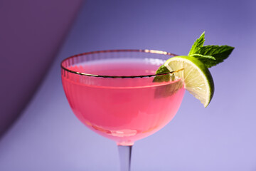 Glass of tasty Cosmopolitan cocktail with mint and lime on purple background