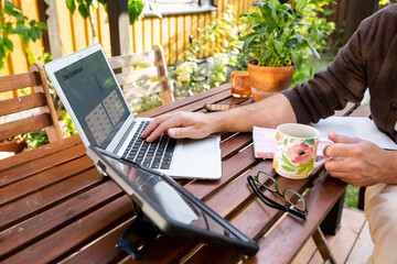 Middle aged man working remotely on laptop at cozy sunny patio, digital nomad lifestyle, outdoor home office, freelance and productivity concept