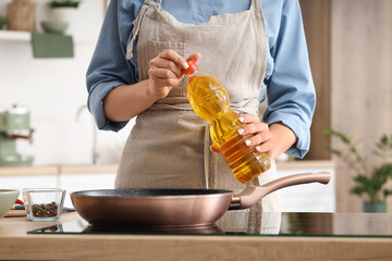 Young woman with sunflower oil near frying pan in kitchen