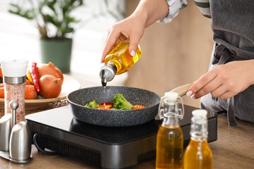 Woman frying vegetables with sunflower oil in kitchen, closeup