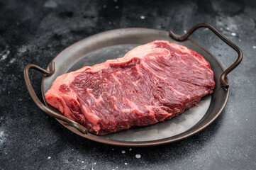 Beef raw sirloin cut or strip loin  with herbs and seasoning on iron pan against rough dark background ideal for recipe blogs grilling menus and cuisine visuals