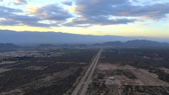 Sunrise over a valley road cutting through on deserted terrain with distant mountains under moody sky, Av. la Mexicana, Chilecito, La Rioja Province, Argentina
